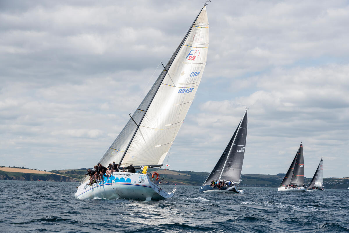 A fleet of racing yachts under full sail on Roaringwater Bay off the West Cork coast, crew hiking out on the rail with the mainland headlands in the distance