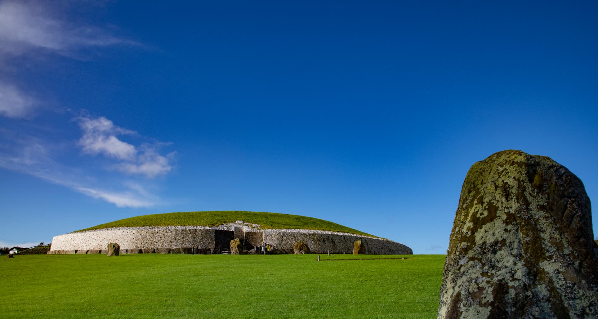 The Neolithic passage tomb at Newgrange, County Meath, with its grass-covered mound and quartz facade under a bright blue sky