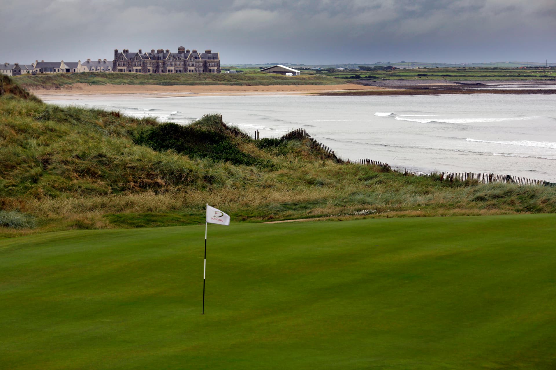 The links course at Trump International Golf Links & Hotel Doonbeg, with the resort's stone hotel above the dunes and the Atlantic beyond