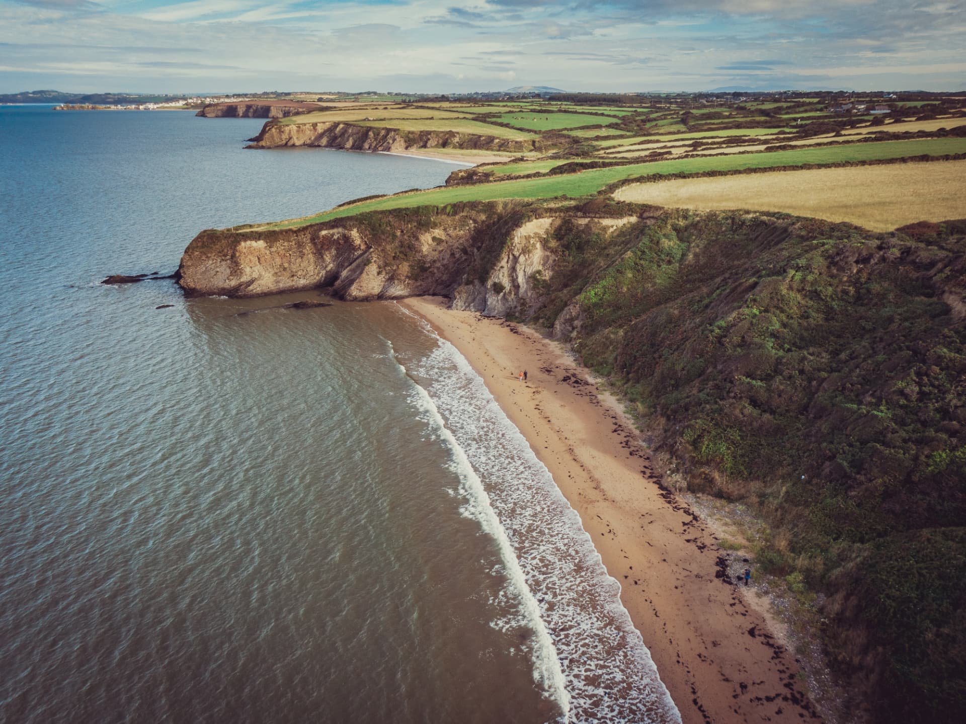 Aerial view of the Ring of Hook coastline in County Wexford, with cliffs, a sandy beach and green farmland running down to the Celtic Sea