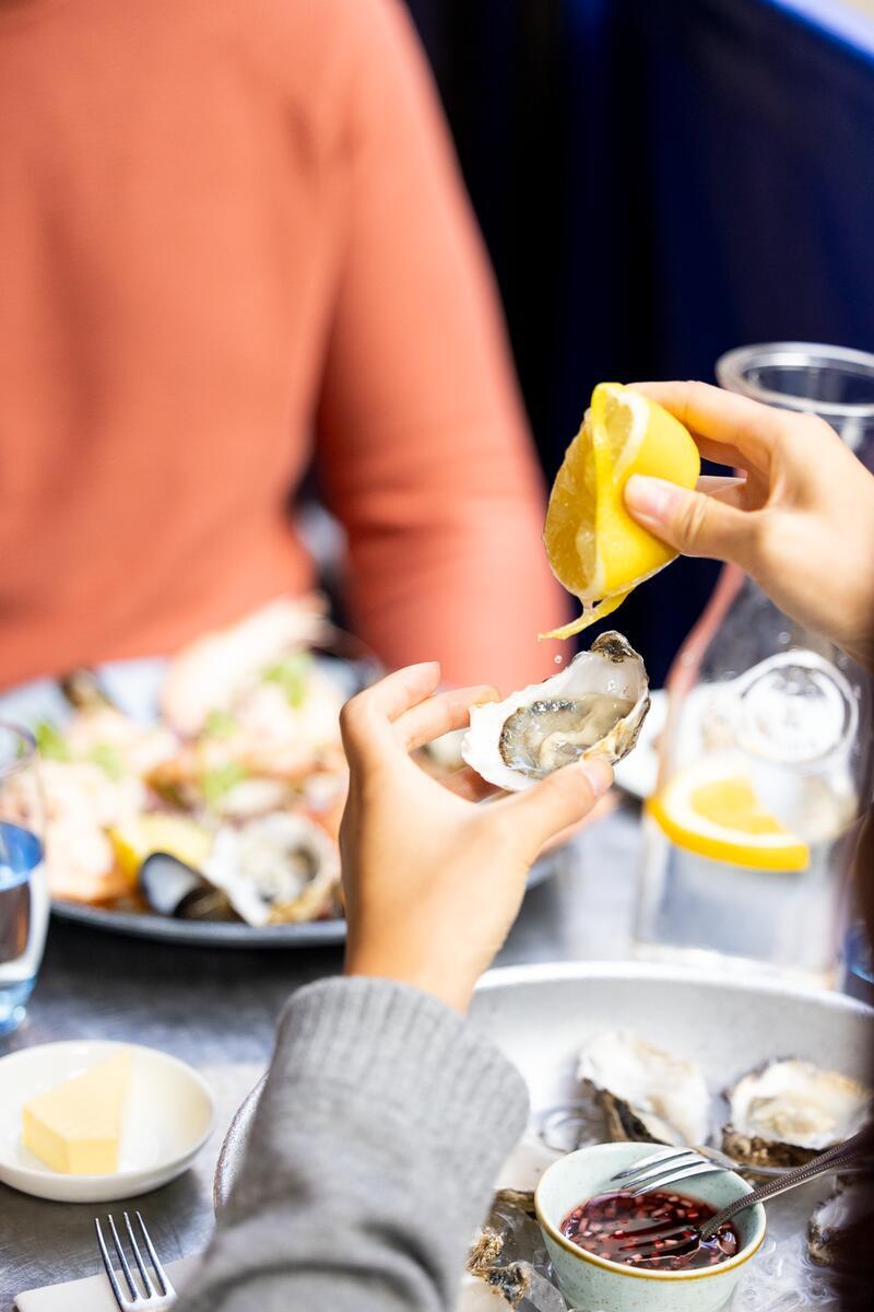 Diner squeezing lemon over a freshly shucked Galway Bay oyster at a seafood table