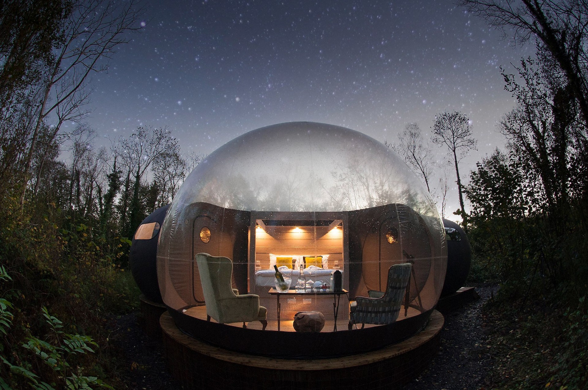 A transparent bubble dome glowing warmly beneath a star-filled sky in the woodland at Finn Lough, County Fermanagh