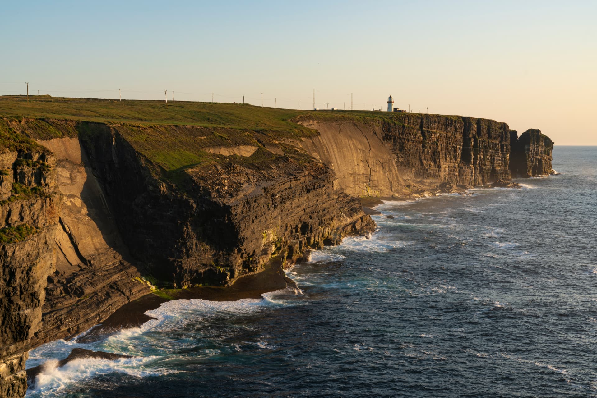 Loop Head Lighthouse standing above layered sea cliffs on the Clare coast near sunset